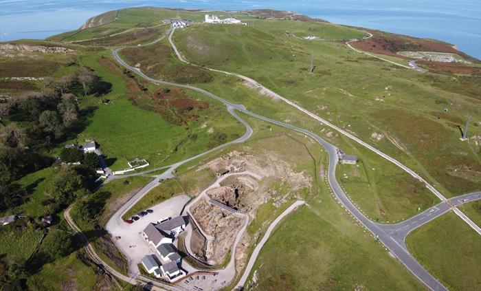 An aerial view, immediately below is the mine which looks like a beige landscape and white buildings that stand out from the green landscape beyond. B